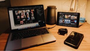 A workstation with a laptop open to an online social platform, an iPad, a cell phone, and a watch