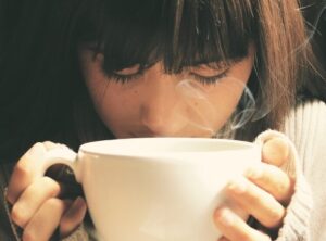 A girl with her nose up to a coffee cup using a self-soothing skill to decrease judgements, especially toward herself