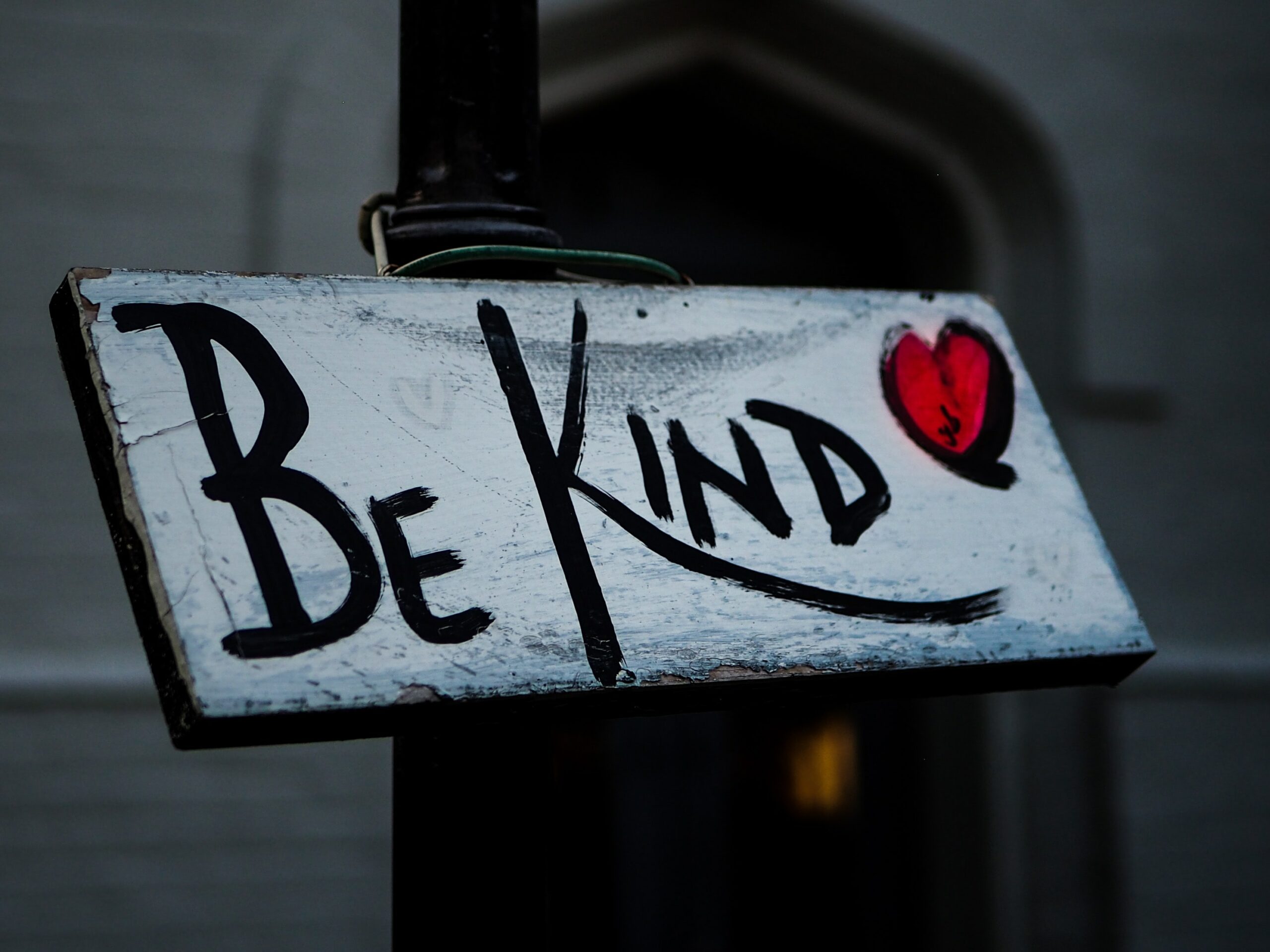 The words "Be Kind" painted on a wooden sign, followed by a heart