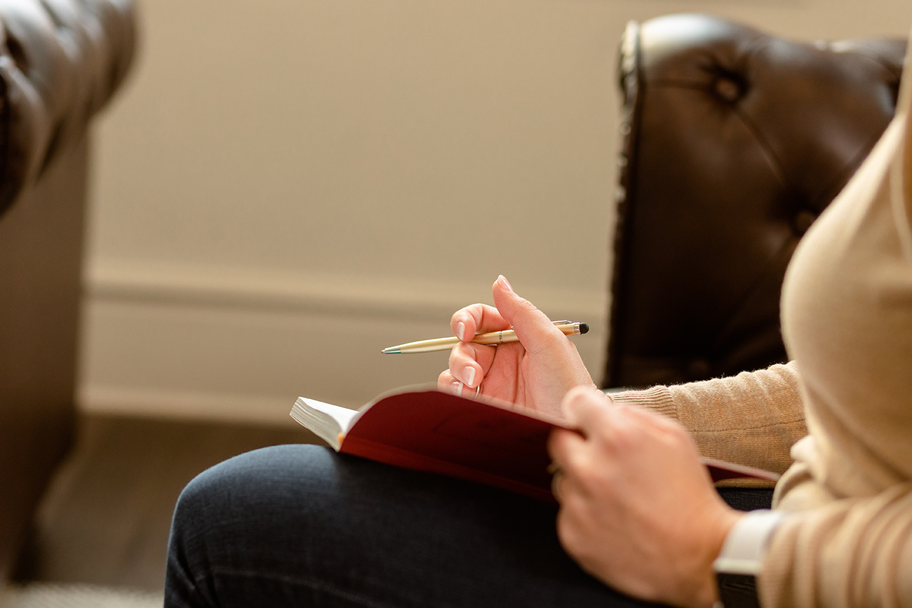 Pink notebook rests in a clinician's lap as they take notes during an individual CBT therapy session for depression