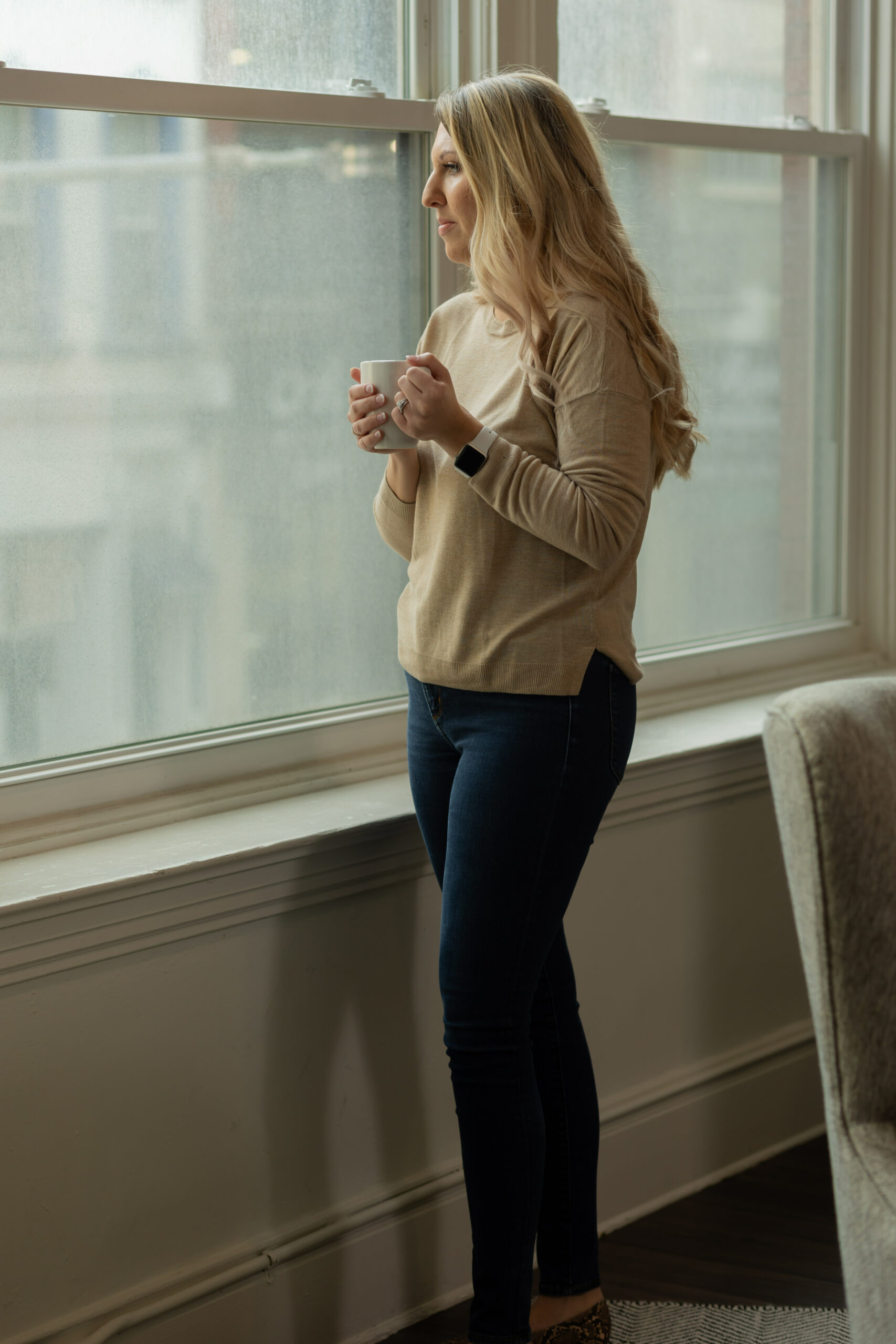 Desirae Allen, DBT psychologist, looks out the window on a dreary day while holding a coffee cup, preparing for a DBT session with a client diagnosed with borderline personality disorder (BPD).