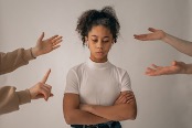 Teen looking down with arms crossed, parents' disapproving hands surrounding her