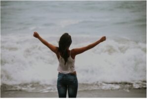 Girl standing with arms open wide standing in front of the ocean