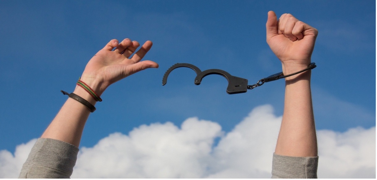 One arm in handcuffs with the other arm breaking free from handcuffs; blue sky in the background