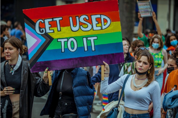 Two people holding a rainbow sign that reads "GET USED TO IT"