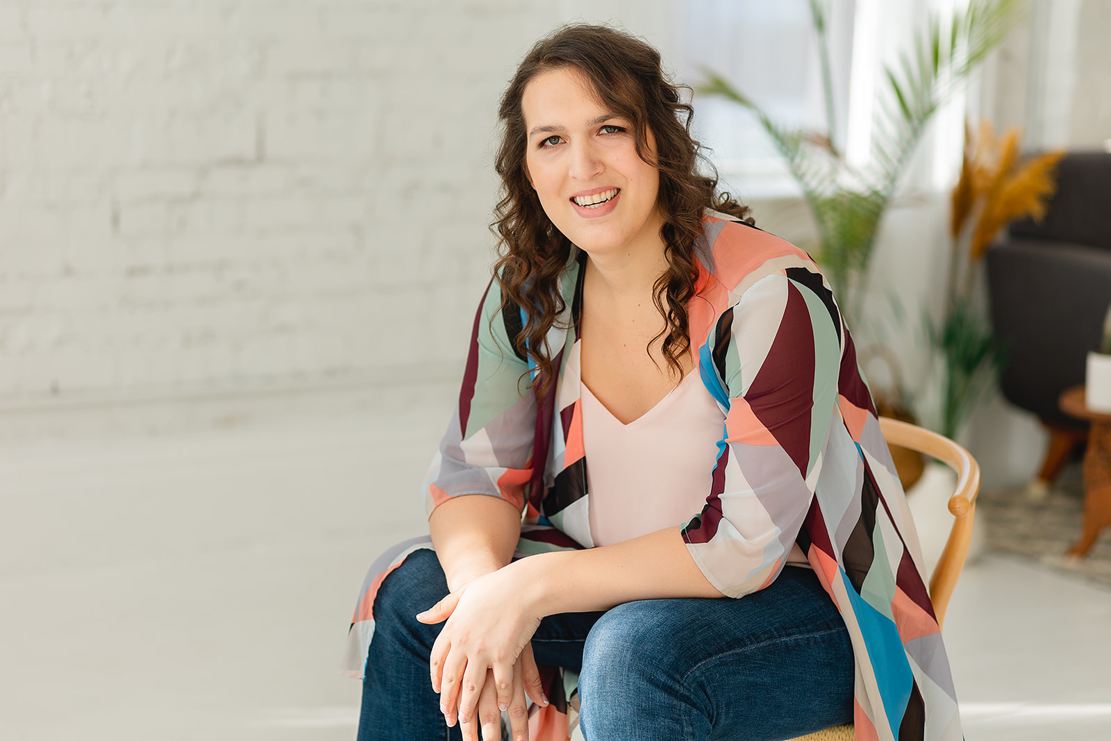 Trans psychologist and LGBTQIA+ DBT therapist in Cincinnati sits in a powerful pose on a chair with her hands crossed. SHe is wearing a cardigan representing the transgender flag.