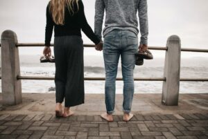 couples standing holding hands in one hand and shoes in another standing by ocean dbt couples therapy