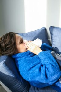 Person sick blowing their nose in a robe laying on the couch