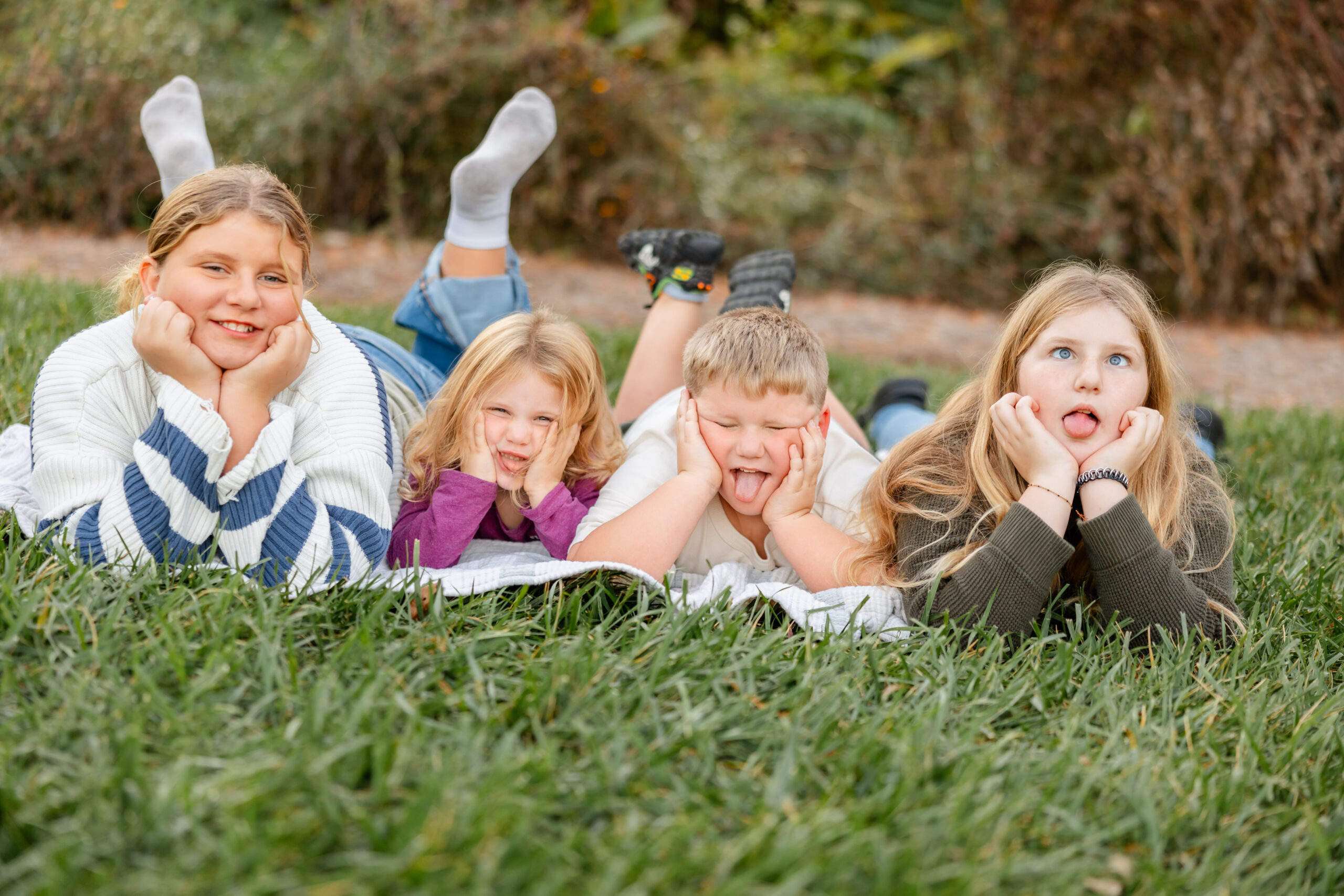 Kids-therapy Four children of varying ages lay on the grass with their heads in their hands making funny faces at the camera, indicating healthy, communicative, emotionally regulated children.