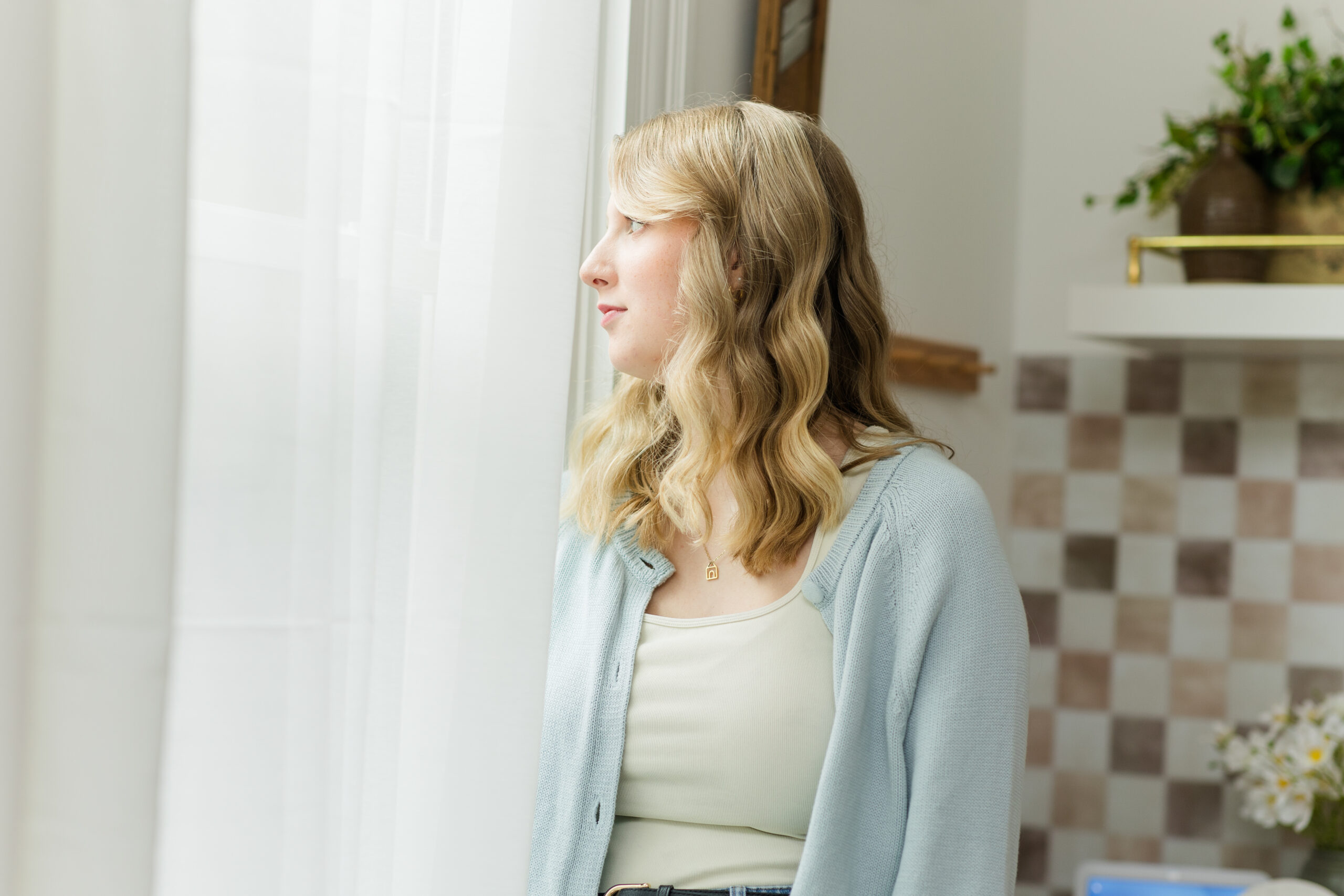 Blonde woman with trauma and PTSD looks out the window with sun on her face after receiving trauma therapy or PTSD therapy