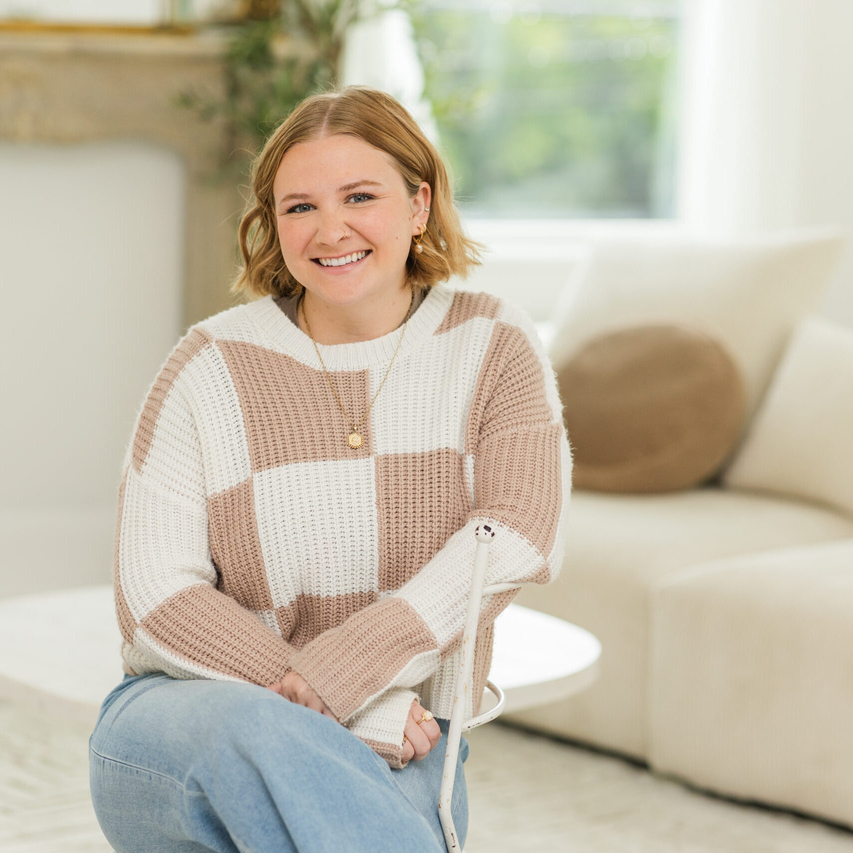 Cincinnati DBT Therapist Catherine Perry sits wearing a checkerboard sweater and blue jeans with legs crossed
