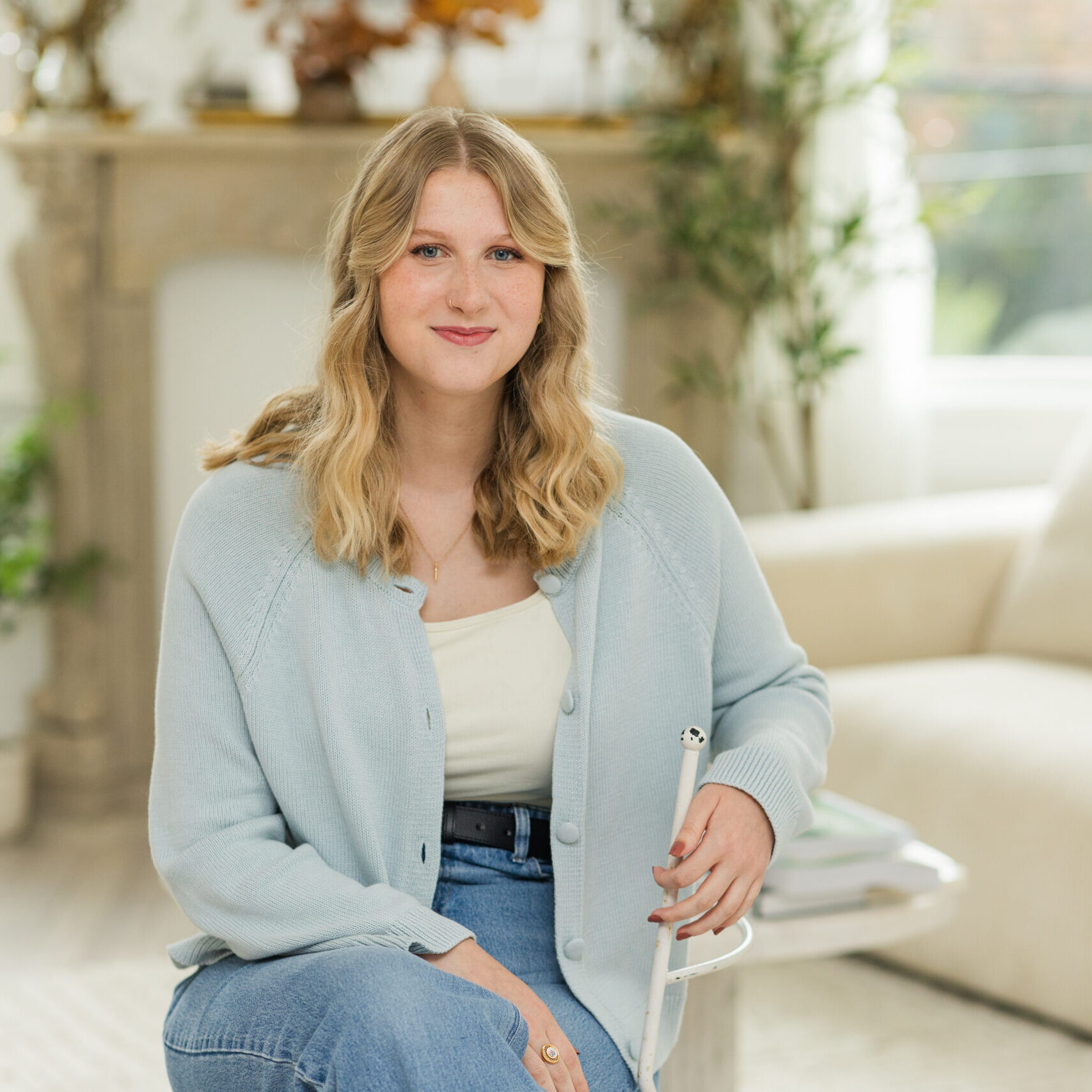Cincinnati DBT Therapist and Admin Kira Waltz wears a white top covered by blue cardigan and jeans while sitting and smiling